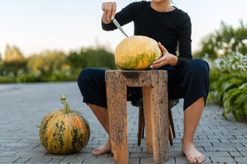 Woman carving pumpkin sitting on wooden stool in the garden