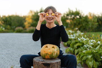 Young woman holding pieces of pumpkin rind like eyeglasses while carving a jack o' lantern
