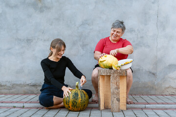 Fototapeta premium Two women carving pumpkins for Halloween party decoration are having fun