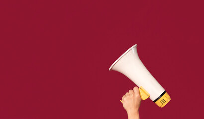 Person holds megaphone against a vibrant red background, ready to make an announcement or call for...