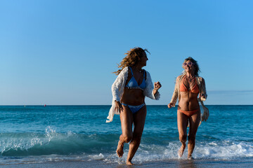 Fototapeta premium Two mature women running on the beach, enjoying summer vacation