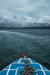 View from ferry boat with rope on deck, leaving white water trail across turquoise sea under cloudy...