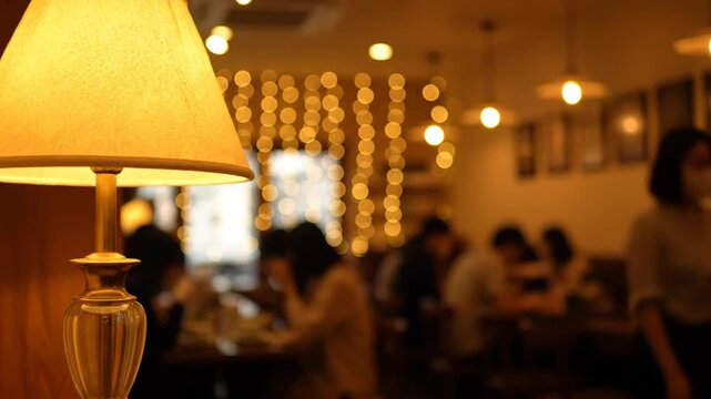 Lamp Sits on Table, People Dine at the Cafe During Early Evening Under Soft Lighting and String Lights, Creating Warm Atmosphere