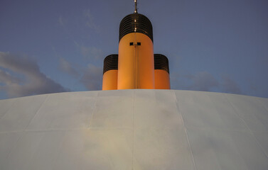 Yellow and black painted funnel smoke stack of luxury cruiseship cruise ship liner against blue sky