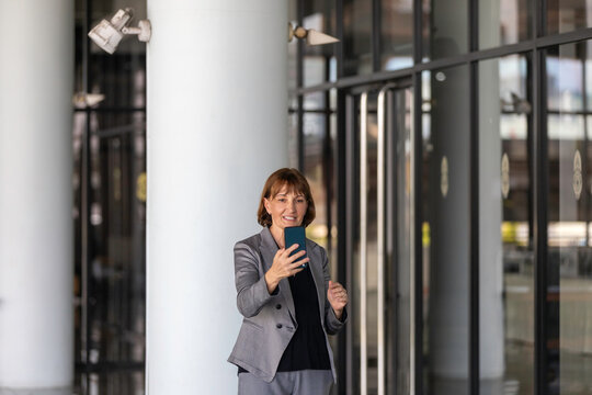 Senior female manager uses her mobile phone to have live communication with clients or family members. Elderly supervisor has a live streaming to discuss with her team member. Technology for business