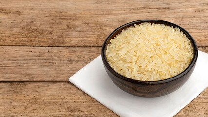 Wooden bowl of uncooked rice on rustic table.