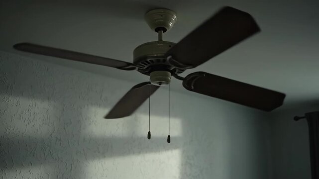 A ceiling fan with four blades is centered in a dimly lit room with textured walls