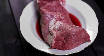Freshly cut beef on a white plate with juices, ready for cooking or preparation in a kitchen setting