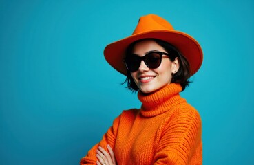 Woman wearing orange hat and sweater smiling with crossed arms against a blue background