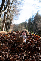 Child playing with fallen autumn leaves in a sunny forest during fall season