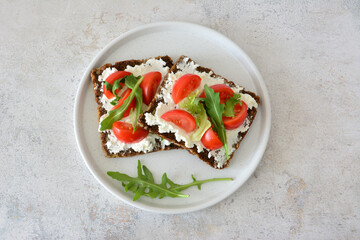 Tomato and ricotta rye bread sandwiches on a white plate with arugula