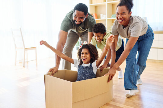 Famili of four, Father and mother  pushing their son and  daughter sitting in a cardboard box, having fun at home. Relocation, new home, family concept