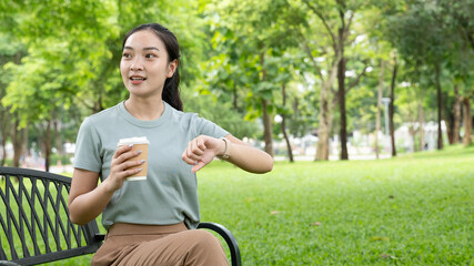 young Asian woman relaxing in a park, drinking a cup of coffee while surrounded by beautiful nature