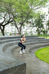 Fototapeta premium Young woman stretching legs and listening music with headphones in the park