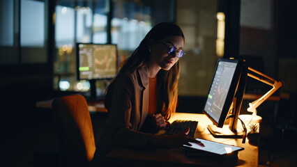 Late economist analyzing charts on desktop screen at night hours business center
