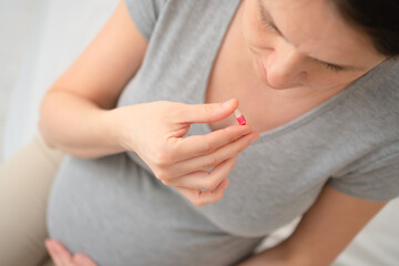Pregnant woman holding a pill in her hand. Top view close-up, focus on medication and care during pregnancy.