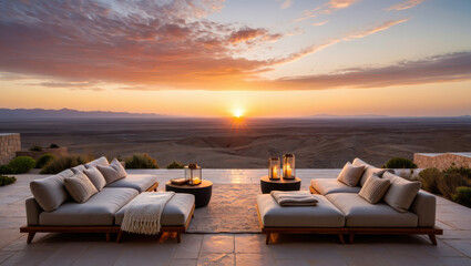 Outdoor lounge area with sofas and lanterns overlooking a desert landscape at sunset time of day