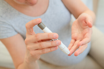 Pregnant female carefully performing self-blood sugar test with digital glucometer. Crucial health monitoring for mother and baby wellbeing.