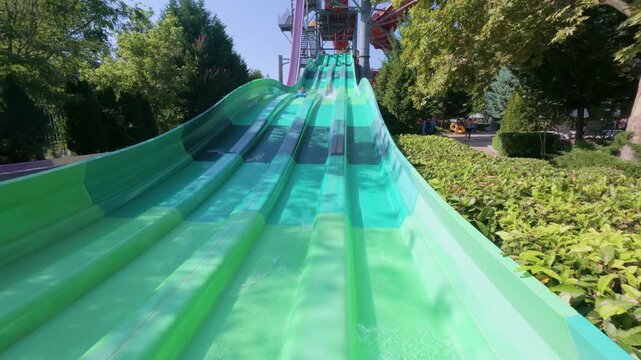 Two kids racing down parallel water slides on blue mats at a water park. Action-packed summer moment full of fun, laughter, and speed under the sun