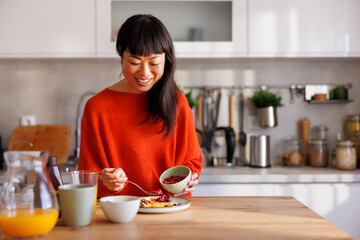 Woman adding berries to waffles while having breakfast at home