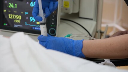 Medical professional wearing blue gloves injecting medicine with a syringe to a patient lying in a hospital bed, with vital signs monitor in the background - Powered by Adobe