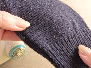 Closeup of woman hands holding dark blue sweater with pills. Sweater cuff with pills, also known as...