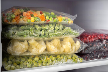 Plastic bags with different frozen vegetables and berries in refrigerator.  Winter supply food in zip bags, preserving nutrients. Vegetables on the freezer shelves.
