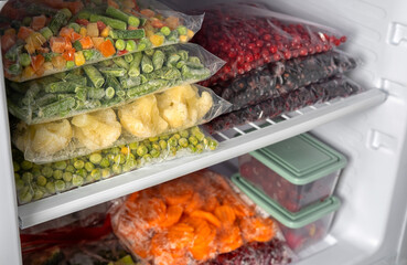 Plastic bags with different frozen vegetables and berries in refrigerator.  Winter supply food in zip bags, preserving nutrients. Vegetables on the freezer shelves.