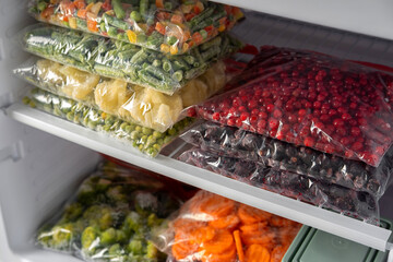 Plastic bags with different frozen vegetables and berries in refrigerator.  Winter supply food in zip bags, preserving nutrients. Vegetables on the freezer shelves.