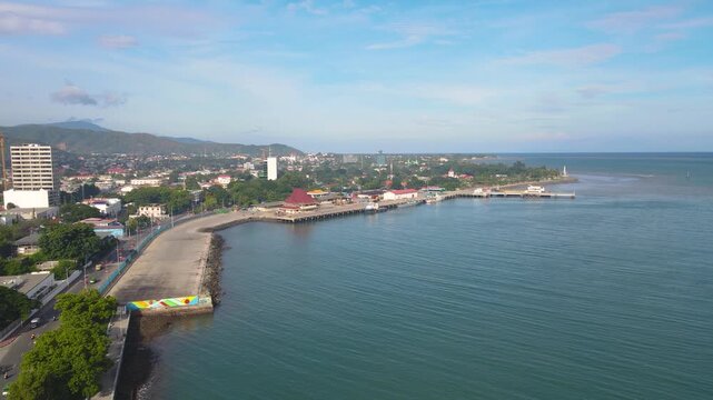 A beautiful aerial view of the capital city of Dili, Timor-Leste. The coastline, Dili Port, and the city blend with the calm blue sea on a sunny day.