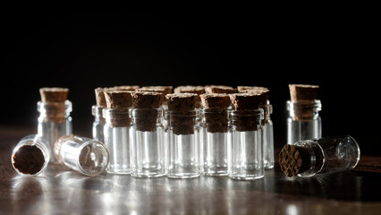 Row of tiny clear glass vials with cork stoppers on a dark table; empty sample bottles for lab...