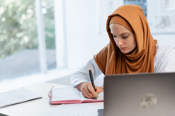 Muslim female doctor with stethoscope working with writing notes of patient and diagnosis with...
