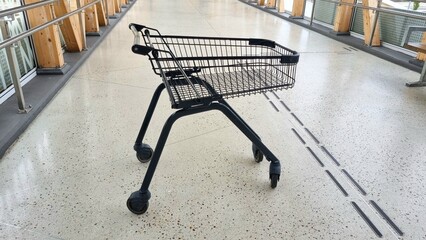 close-up of metal grocery cart with black handles for shopping on cement floor in store, business...