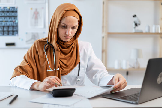 Muslim female doctor with stethoscope working in hospital use calculator and laptop