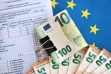 European euro currency money notes bunch on tax form and European union blue flag close up