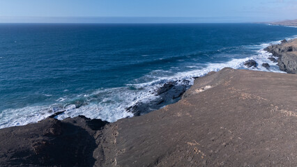 Rocky coastline with powerful waves crashing against rugged cliffs under a clear sky, showcasing...