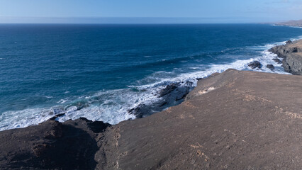 Rocky coastline with powerful waves crashing against rugged cliffs under a clear sky, showcasing...