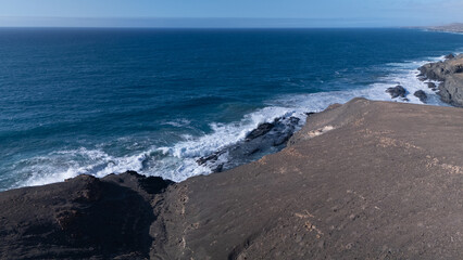 Rocky coastline with powerful waves crashing against rugged cliffs under a clear sky, showcasing...