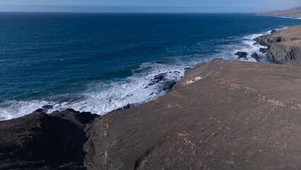 Rocky coastline with powerful waves crashing against rugged cliffs under a clear sky, showcasing...
