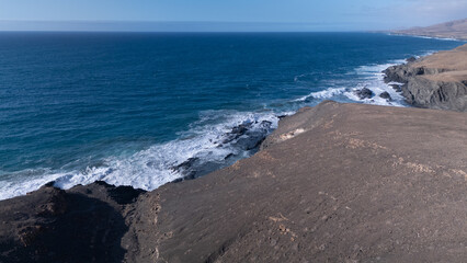 Rocky coastline with powerful waves crashing against rugged cliffs under a clear sky, showcasing...