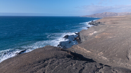 Rocky coastline with powerful waves crashing against rugged cliffs under a clear sky, showcasing...
