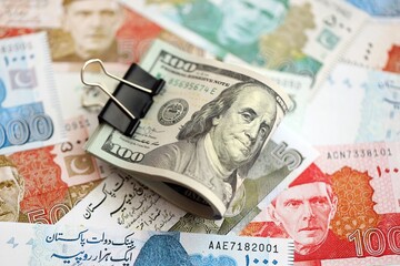 Roll of US dollar bills lies on big amount of Pakistan rupees banknotes close up