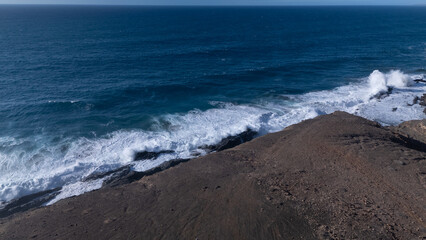 Rocky coastline with powerful waves crashing against rugged cliffs under a clear sky, showcasing...