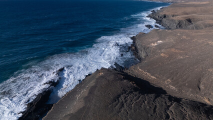 Rocky coastline with powerful waves crashing against rugged cliffs under a clear sky, showcasing...