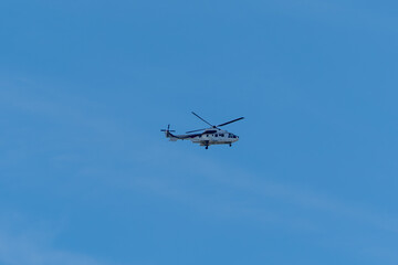 A helicopter flies across the clear blue sky. Its white body contrasts with the bright background.