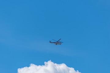 A helicopter hovers above white clouds in a blue sky. The aircraft is seen in mid-flight.