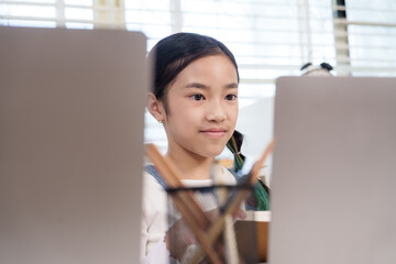 Asian preteen girl concentrating while working on laptop during classroom activity representing...
