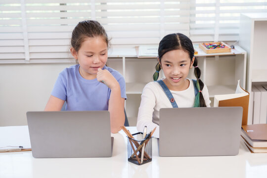 Asian preteen girl using laptop smiling while studying with caucasian friend during classroom teamwork activity representing education creativity digital learning friendship modern school project - Powered by Adobe