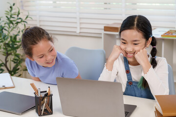 Caucasian schoolgirl laughing while asian preteen classmate using laptop classroom teamwork project...