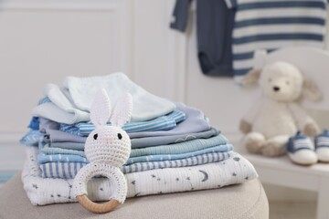 Stack of clean baby clothes and toy on pouf indoors, closeup